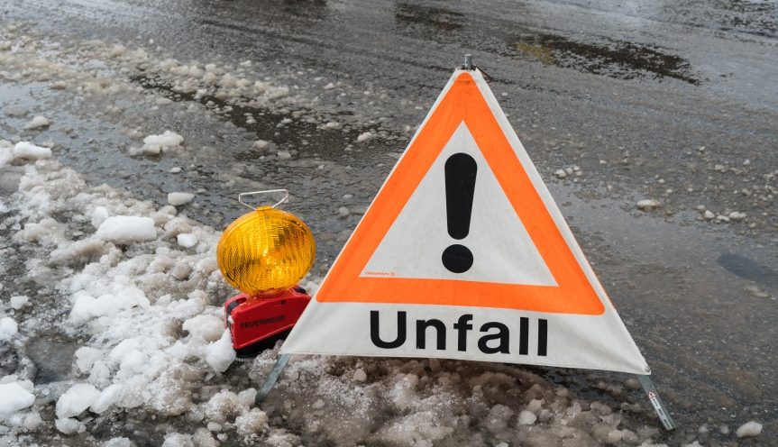 Warnschild Unfall und Warnleuchte an einer Straße mit Schneematsch.